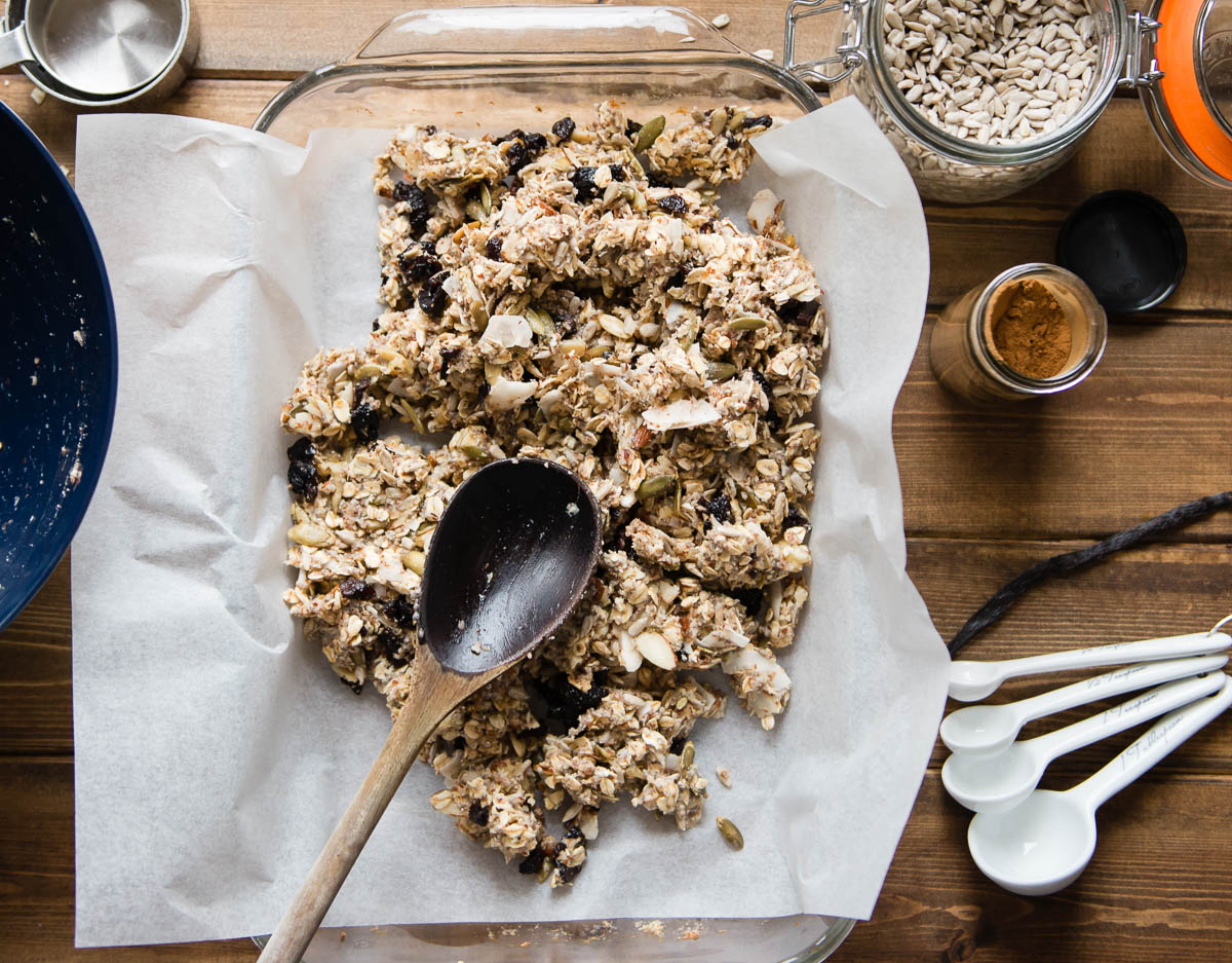 pushing the vegan protein bar mixture into a glass baking dish lined with parchment paper, using a wooden spoon.