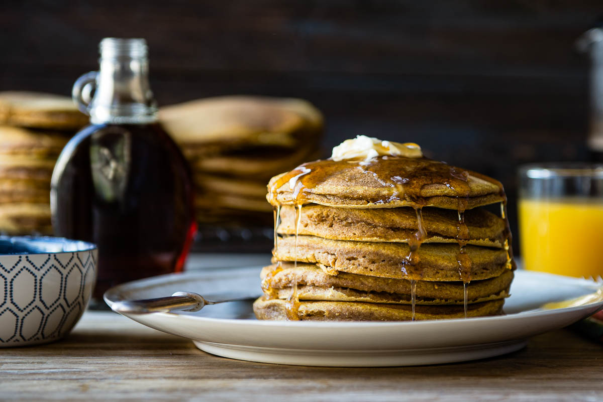 stake of vegan pumpkin pancakes drizzled with maple syrup and topped with a pat of vegan butter on a plate.