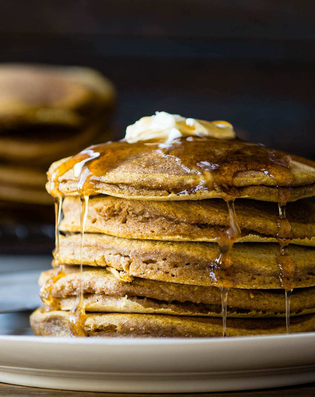 stack of pancakes on a white plate covered in maple syrup.