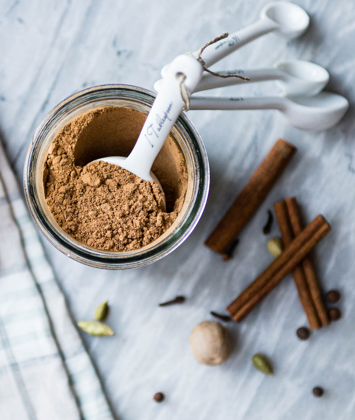 glass jar full of homemade pumpkin pie spice with a white tablespoon measurement scooping out some.