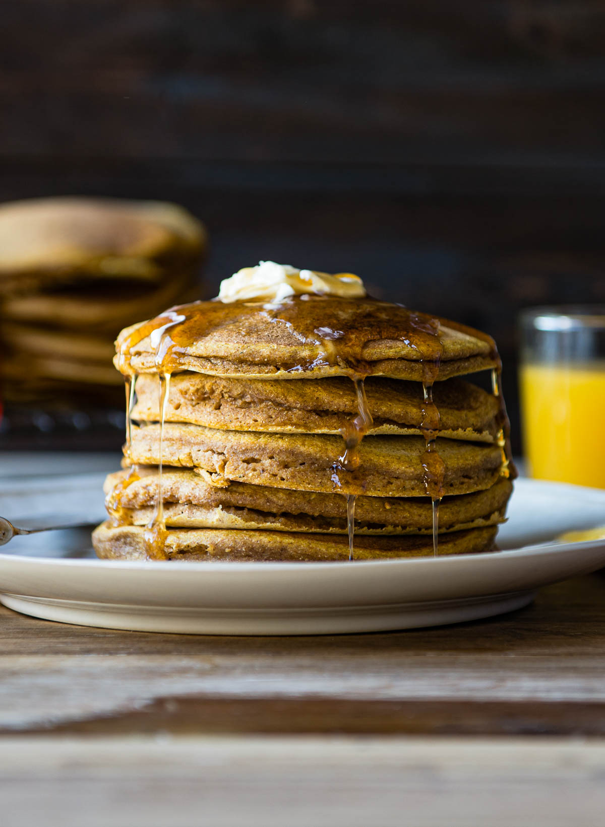 stack of pumpkin pancakes on a plate with maple syrup and vegan butter on top. 