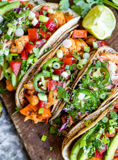 several vegetarian tacos in a row on a wooden board.