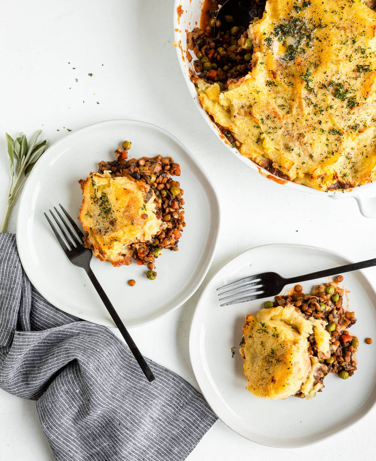 2 white plates with 1 serving each of shepherd's pie with lentils and black forks.