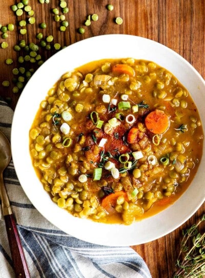 Vegetarian split pea soup in a white bowl next to a spoon on a blue striped tea towel.