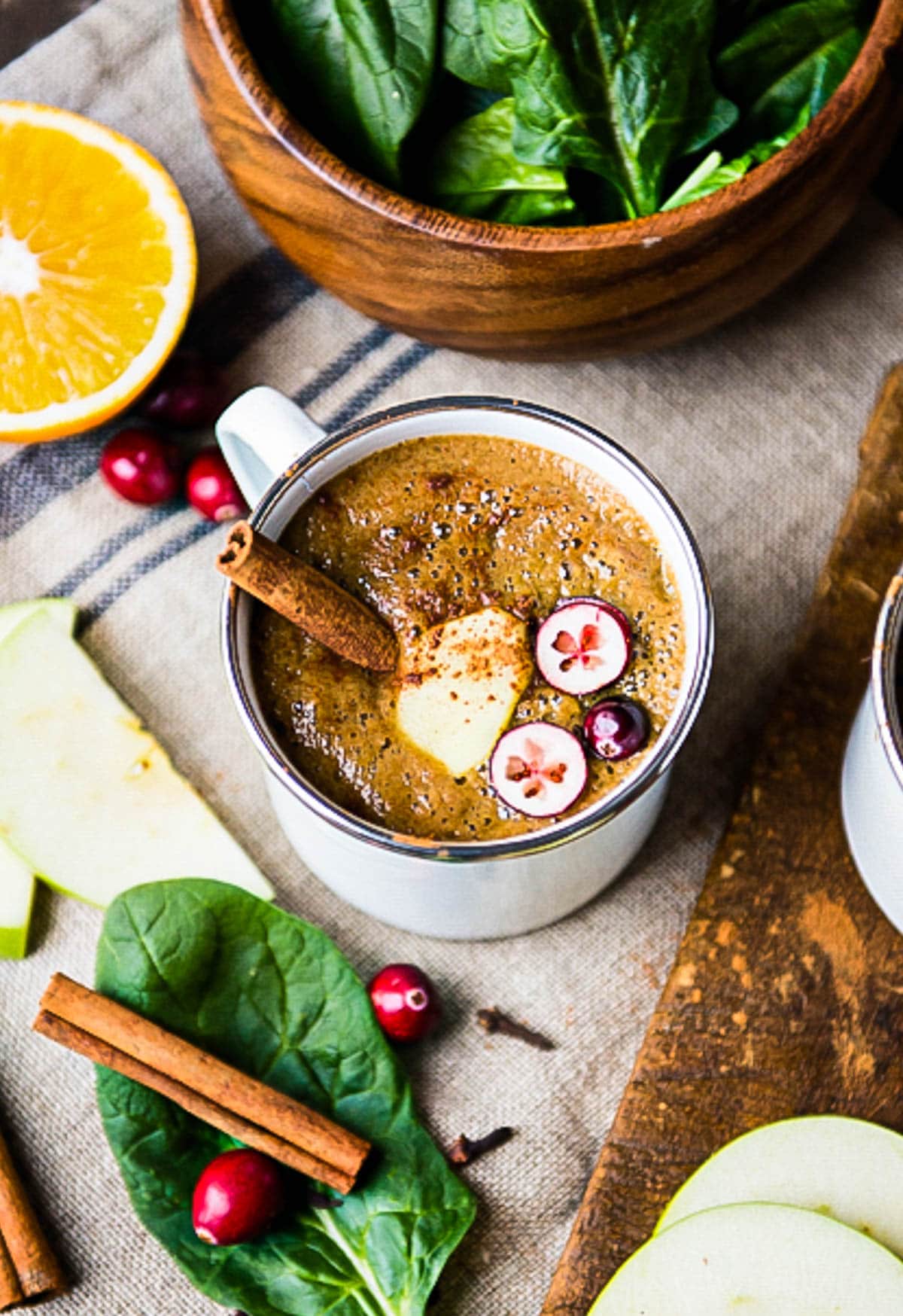 warm winter smoothie topped with apple slices, cranberries and a cinnamon stick in a white mug.