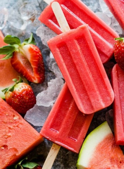 fresh watermelon popsicles sitting on ice with fresh strawberries and watermelon slices.