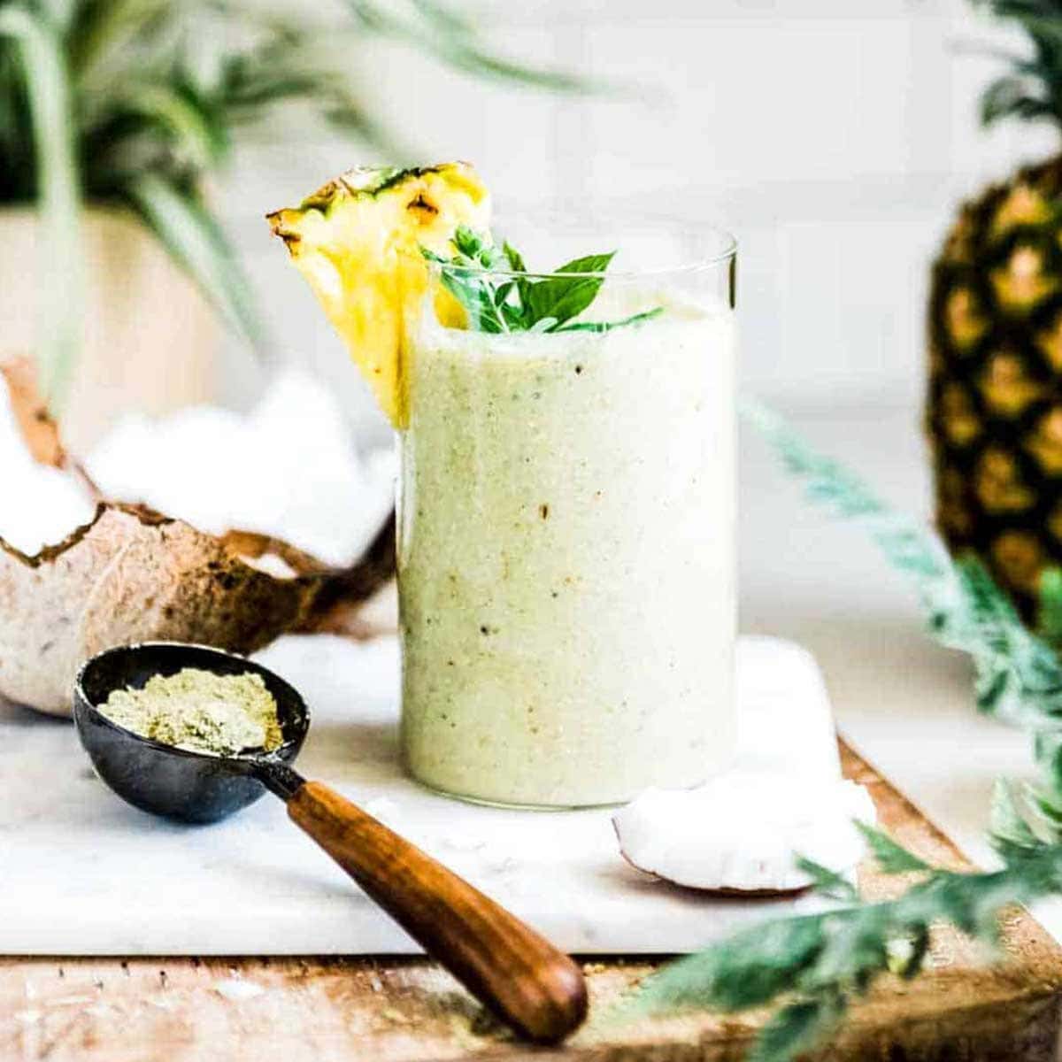 weight gain smoothie in glass with fresh pineapple and mint on top, next to a scoop of protein powder.