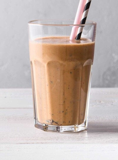 Glass of a delicious chocolate weight loss shake with a pink straw and a black and white striped straw on a light, woodgrain countertop.