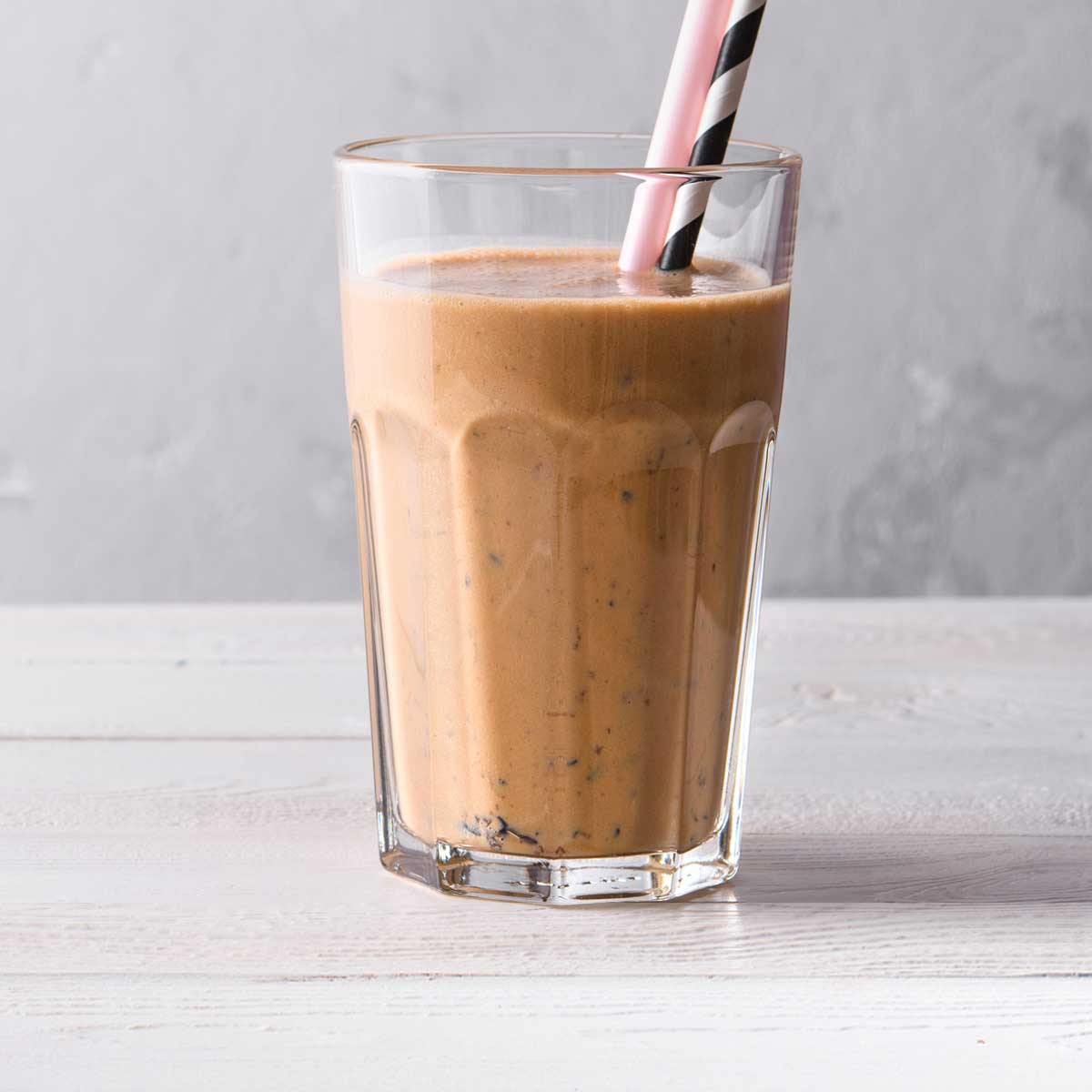 Close-up of a chocolate weight loss shake in a glass with a pink straw and a black-and-white striped straw.