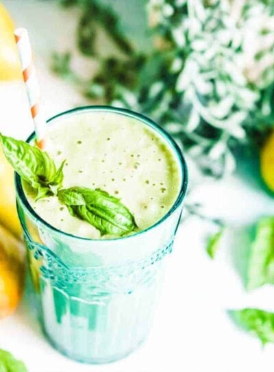 A glass of acid reflux smoothie with a straw, topped with a basil leaf, surrounded by fresh ingredients.