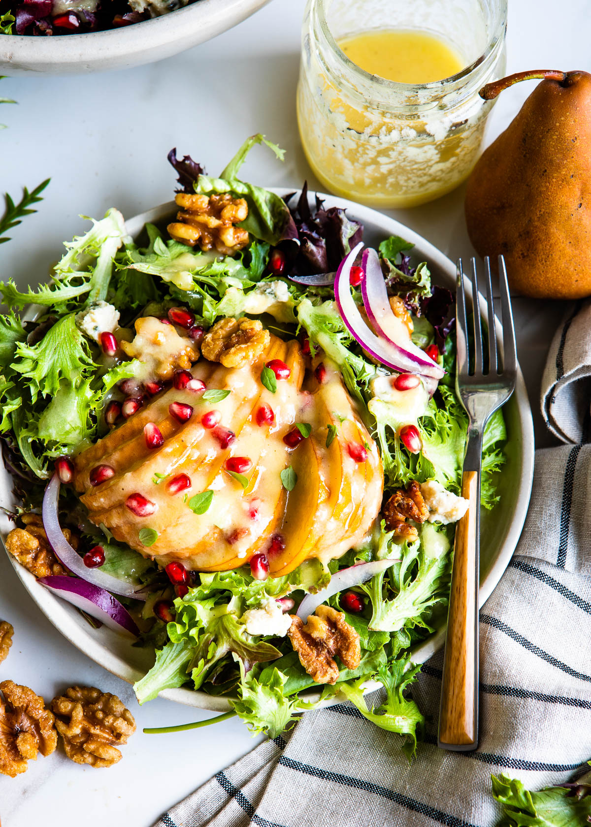 winter pear salad topped with vinaigrette dressing and pomegranate arils on a circle plant with a fork. 