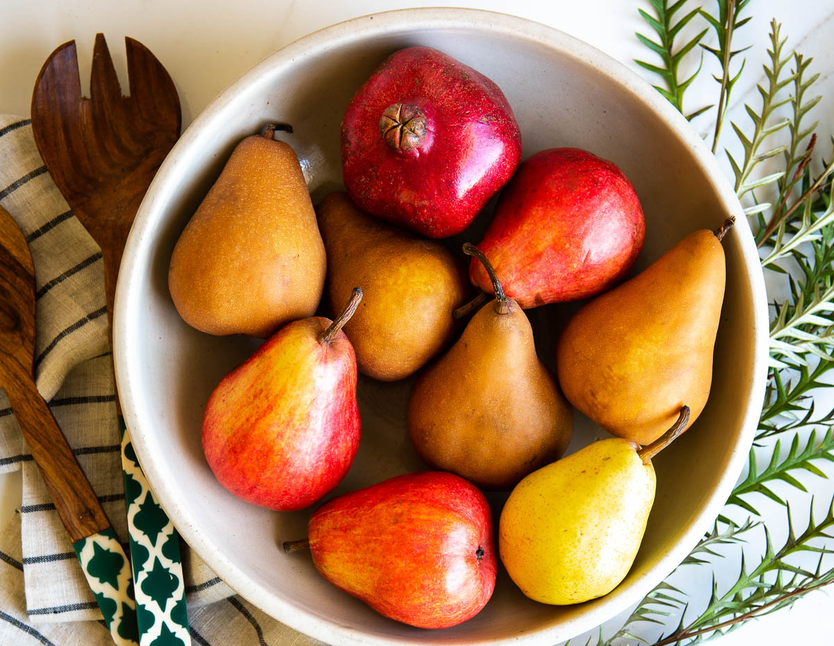 ceramic bowl of pears, some red and some brown, sitting on a striped tea towel. 