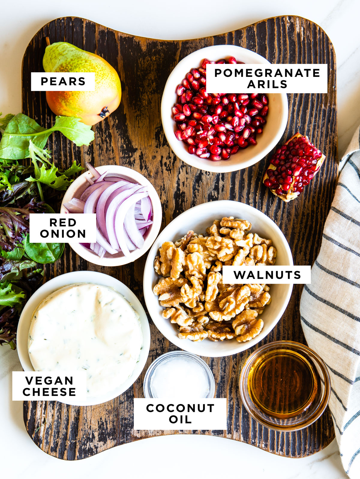 labeled ingredients for a pear salad including pears, pomegranate arils, red onion, walnuts, vegan cheese and coconut oil. 